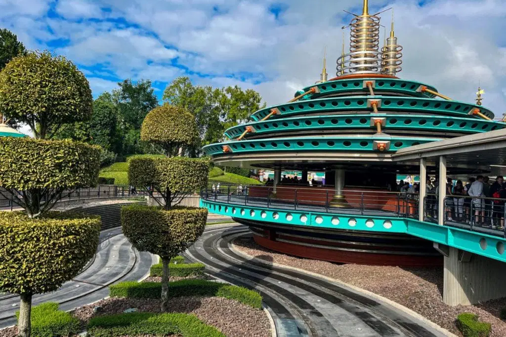 Autopia-1024x683.jpg Futuristic, teal and gold structure with neatly trimmed trees in the foreground, part of a ride at Disneyland Paris.