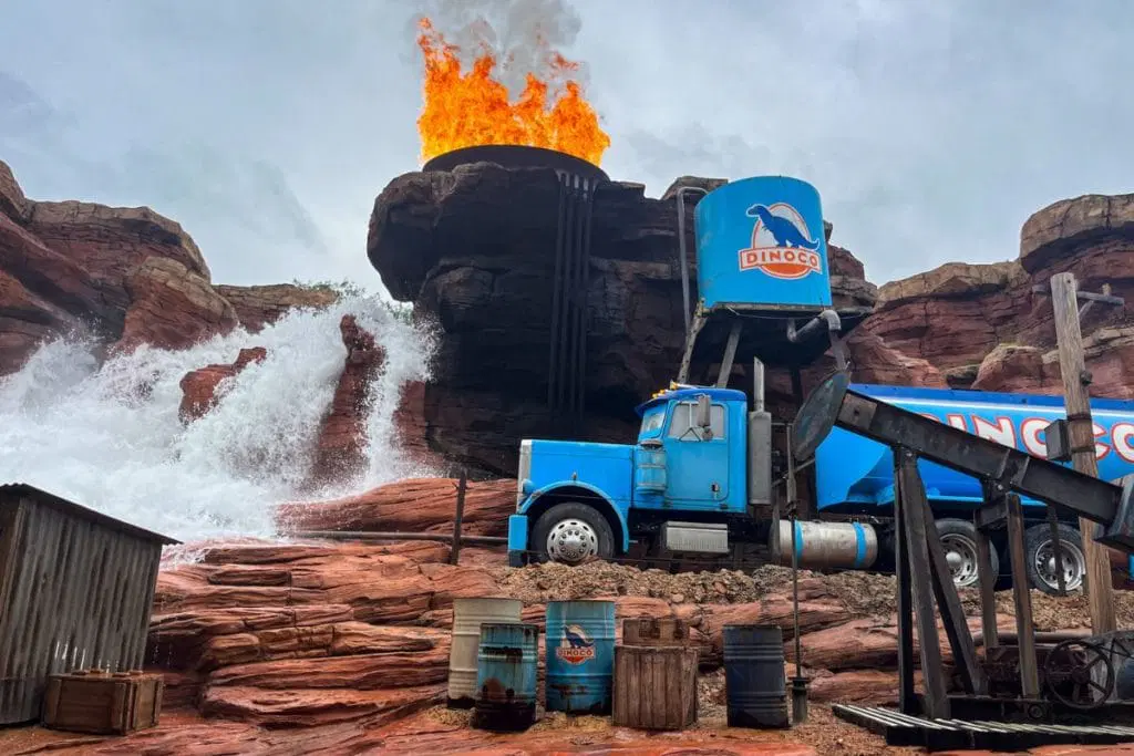 Cars-ROAD-TRIP-1024x683.jpg Scene from the Cars Road Trip attraction featuring a large blue truck with "Dinoco" branding, fake fire, and water effects in a rocky desert setting.