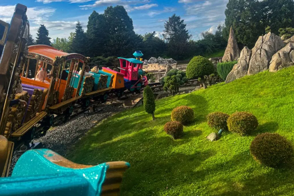 Brightly colored Casey Jr. train winding through a lush, green landscape with whimsical topiary and rocky structures at Disneyland Paris.