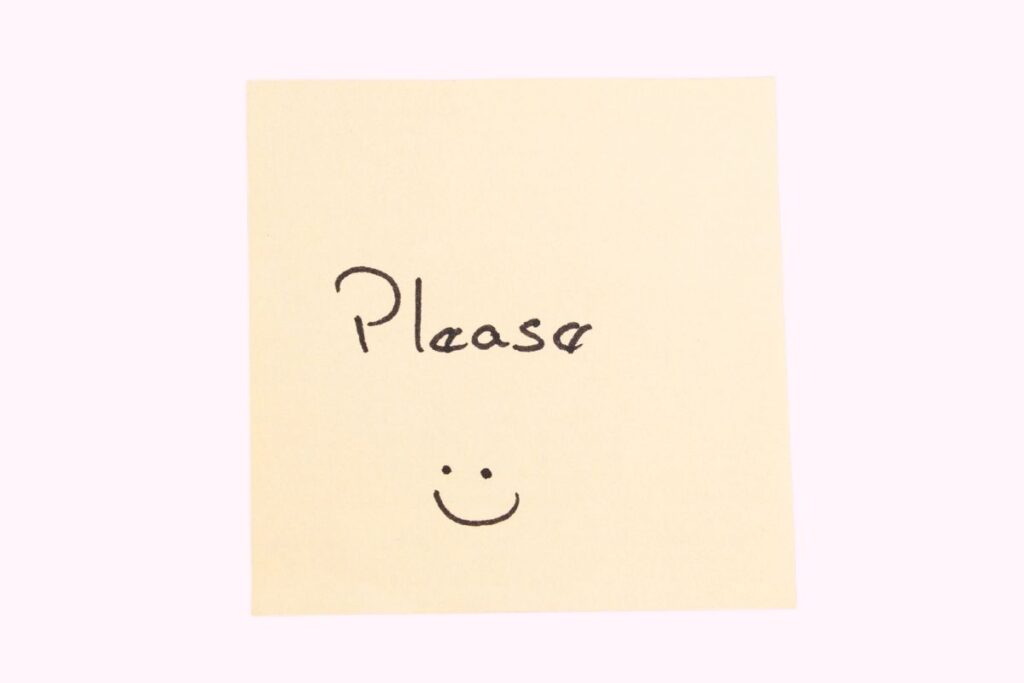 Saying Please This image shows a pale yellow sticky note placed against a soft, light background. Written in black ink on the note is the word “Please,” followed by a small hand-drawn smiley face beneath it. The handwriting is informal and slightly uneven, giving the note a friendly and personal feel. The minimal composition keeps the focus entirely on the message, with no additional objects or distractions in the frame. The smiley face adds warmth and approachability, reinforcing the polite tone of the word. The image conveys kindness, courtesy, and gentle communication, making it suitable for illustrating basic manners, polite requests, or early language learning.